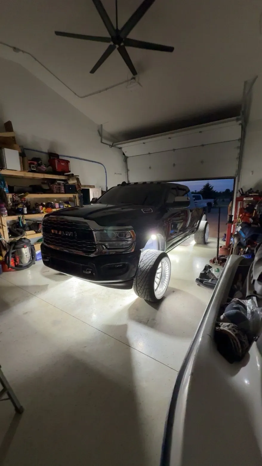 A black RAM 3500 dually on polished wheels inside a garage, white rock lights throwing a pool of light across the floor.