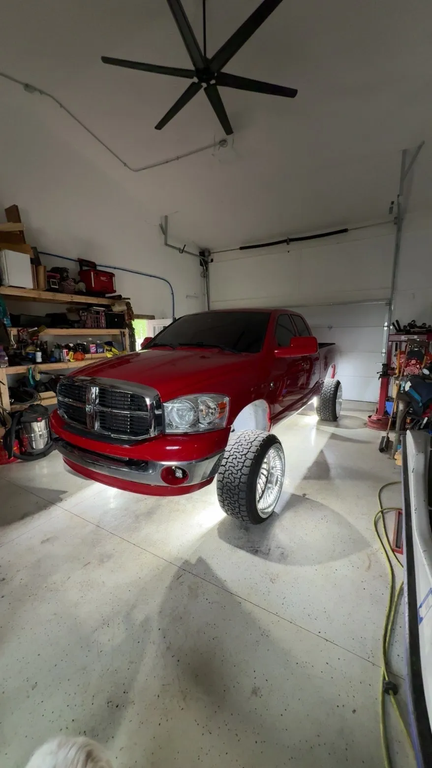 A red Dodge Ram on polished wheels in a garage, rock lights lit beneath the doors.